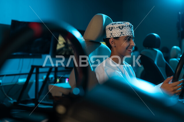 النظر للشاشة المعلقة على الحائط اثناء اللعب , شاب عربي خليجي عماني يرتدي الدشداشة البيضاء و الكمة المطرزة يجلس على كرسي السائق , قضاء اوقات مميزة , صورة مقربة