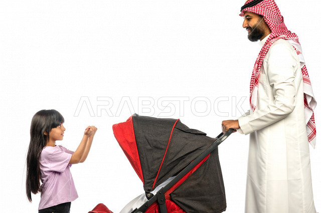 Portrait of a Saudi Arabian Gulf man pulling a stroller with his young daughter with gestures indicating happiness and love, emotional bonding, the concept of a happy family, a family picnic and a tour, spending fun family times