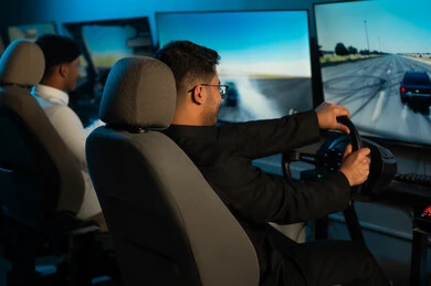 لعبة محاكاة سباق السيارات الحقيقية , شابان عربيان خليجيان سعوديان يرتديان الثوب الابيض و الاسود يجلسان امام الشاشة المعلقة على الحائط , ايماءات السعادة و الفرحة , صورة خلفية , الامساك بمقود اللعبة