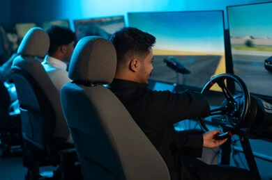 تحريك مقود السيارة يميناًو ياساراً للتحكم في السباق , رجلان عربان خليجيان سعوديان يرتديان الثوب الابيض و الاسود يجلسان امام الشاشة , الحماس و الاصرار على الفوز بالسباق , العاب جماعية ممتعة بين الاصدقاء