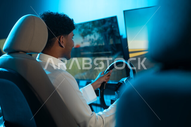 التمسك بالمقود جيداً للسيطرة على السباق , رجل عربي خليجي سعودي يرتدي الثوب الابيض يجلس خلف الشاشة المعلقة , الاصرار على الفوز بسباق السيارات
