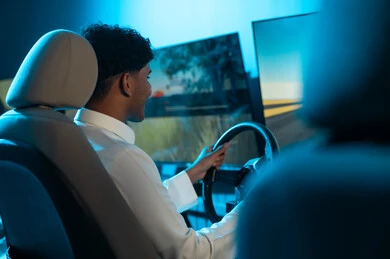 التمسك بالمقود جيداً للسيطرة على السباق , رجل عربي خليجي سعودي يرتدي الثوب الابيض يجلس خلف الشاشة المعلقة , الاصرار على الفوز بسباق السيارات