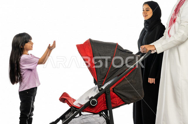 Portrait of a Saudi Arabian Gulf man pulling a stroller with his wife and young daughter with gestures indicating happiness and love, emotional bonding, the concept of a happy family, a family picnic and a tour, spending fun family times