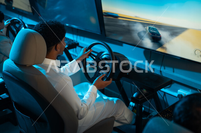 توجيه المحرك يميناً و يساراً للفوز في السباق , رجل عربي خليجي سعودي يرتدي الثوب الابيض يلعب لعبة السيارات , النظر الي الشاشة المعلقة , صورة خلفية