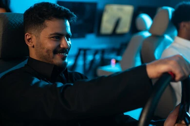 Happiness for winning first place in the car game, an Arab Gulf Saudi man wearing a black thobe sits behind the game steering wheel, simulating real driving, moments of fun and entertaining time, gestures of smiles and joy.