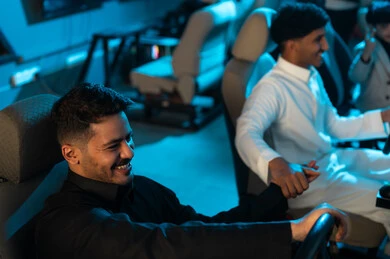 Sharing enjoyable moments with friends inside electronic gaming centers, two Arab Gulf men from Saudi Arabia wearing white and black thobes holding each other's hands, excitement and joy while playing, determination to win the race.