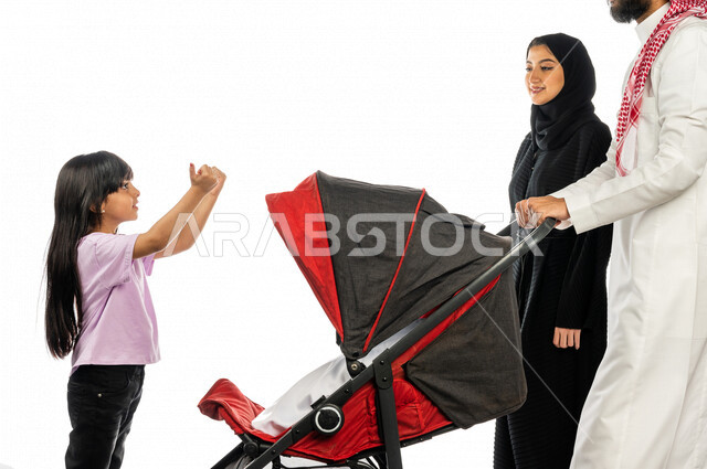 بورتريه لرجل عربي خليجي سعودي يجرعربة الأطفال برفقة زوجته و ابنته الصغيرة بإيماءات تدل على السعادة و المحبة ، ترابط عاطفي ، مفهوم الأسرة السعيدة ، نزهة و جولة عائلية ، قضاء أوقات عائلية ممتعة