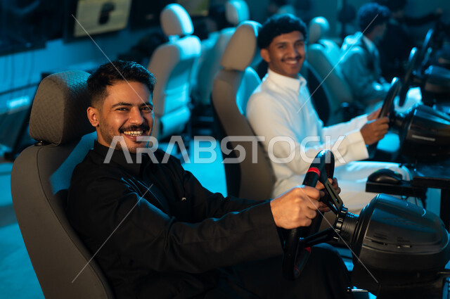 النظر للكاميرا بابتسامة , رجلان عربيان خليجان سعوديان يرتديان الثوب الابيض و الاسود , صورة مقربة , الجلوس على الكراسي خلف مقود السيارة , لعبة محاكاة للقيادة الحقيقية