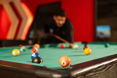 كرات صغيرة مرقمة ملونة على طاولة البلياردو الخضراء , صورة مقربة , رجل عربي خليجي سعودي يرتدي الثوب الاسود , تحريك الكرة البيضاء لبداية اللعبة , كرة برتقالية رقم ثمانية