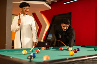 توجيه العصا الخشبية للكرة البيضاء الصغيرة , رجل عربي خليجي سعودي يرتدي الثوب الابيض ينظر الى صديقه بسعادة , مشاركة الاصدقاء اللحظات الممتعة , ايماءات الفرحة و الابتسامة ,