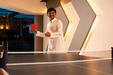 Looking at a friend with happiness and joy before starting the game, a Saudi Arabian Gulf man holding a small table tennis ball, competitive group games among friends inside game centers in the Kingdom.
