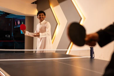 حمل الكرة البيضاء الصغيرة الخاصة بلعبةتنس الطاولة داخل كف اليد , رجل عربي خليجي سعودي يرتدي الثوب الابيض ينظر بابتسامة لصديقه , لحظات مسلية مع الاصدقاء