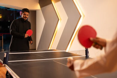 متابعة الكرة بتركيز , رجل عربي خليجي سعودي يرتدي الثوب الاسود يحمل المضرب الخشبي الاحمر الصغير , الروح التنافسية بين الاصدقاء , شاب عربي خليجي سعودي يرتدي الثوب الابيض يحمل الكرة البيضاء