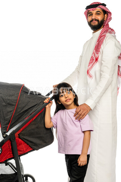 Portrait of a Saudi Arabian Gulf man pulling a stroller with his young daughter with gestures indicating happiness and love, emotional bonding, the concept of a happy family, a family picnic and a tour, spending fun family times