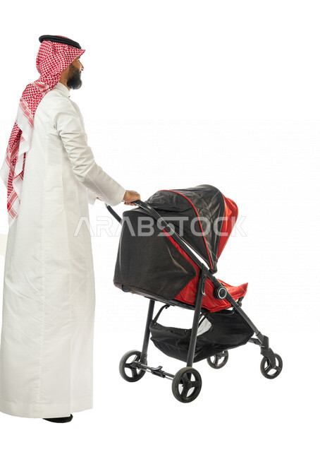 بورتريه من الخلف لرجل عربي خليجي سعودي يجرعربة الأطفال ، رابطة الأبوة ، ترابط عاطفي ، مفهوم الأسرة السعيدة ، نزهة و جولة عائلية ، قضاء أوقات عائلية ممتعة