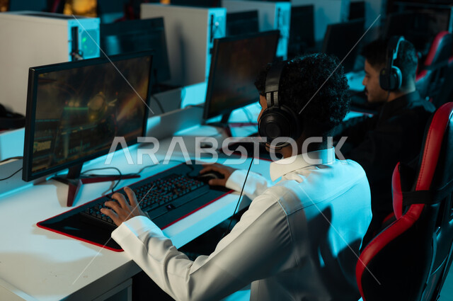 التواصل مع الاصدقاء اثناء اللعب باستخدام  الانترنت , رجلان عربيان خليجيان سعوديان يرتديان الثوب الاسود و ثوب ابيض يجلسان امام شاشة الحاسب المكتبي , التركيز و اللعب بشغف