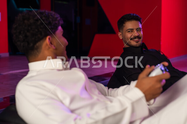 رجلان عربيان خليجيان سعوديان يرتديان الثوب الابيض و ثوب اسود ,النظر لاحدهما الاخر بابتسامة قبل بداية التحدي , انشطة ترفيهية ممتعة فى المملكة , ايماءات السعادة و الفرحة