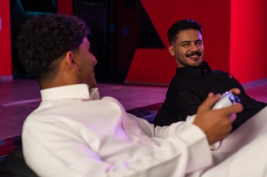 Two Arab Gulf men from Saudi Arabia are wearing a white thobe and a black thobe, looking at each other with a smile before the challenge begins, enjoying fun recreational activities in the kingdom, gestures of happiness and joy.