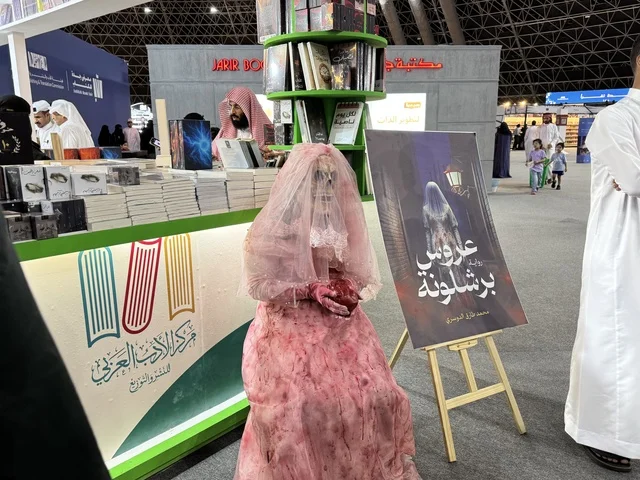 Arab Literature Center, a depiction of a figure wearing a pink wedding dress, a promotional tool for a novel titled "Bride of Barcelona," International Book Fair in Jeddah on December 16, 2025, famous cultural landmarks and tourist attractions in the Kingdom of Saudi Arabia, attracting and drawing tourists from around the world, Riyadh Season events.