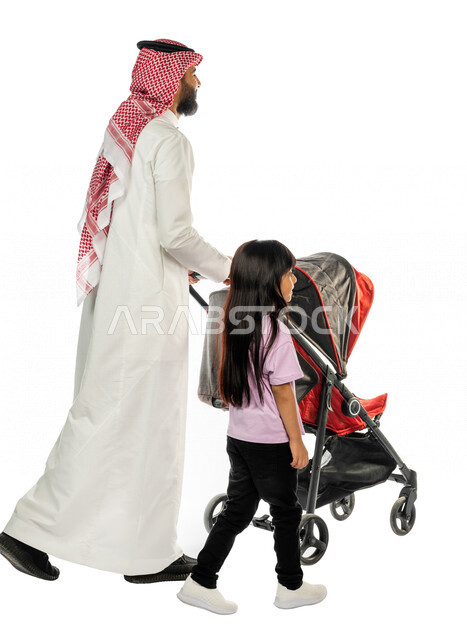 بورتريه من الخلف لرجل عربي خليجي سعودي يجرعربة الأطفال برفقة ابنته الصغيرة بإيماءات تدل على المحبة ، ترابط عاطفي ، مفهوم الأسرة السعيدة ، نزهة و جولة عائلية ، قضاء أوقات عائلية ممتعة