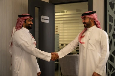 The concept of trust and building professional relationships, cooperation and partnership in the work environment, a successful business meeting, two Arab Gulf men from Saudi Arabia wearing white thobes and shemaghs shaking hands inside the office.