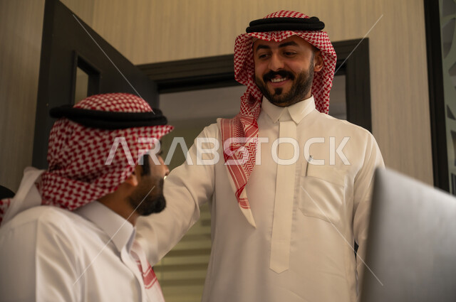 Monitoring the workflow and discussing technical details, teamwork and the spirit of unity, teaching employees new methods of work to achieve the company's goals, two Arab Gulf colleagues from Saudi Arabia wearing the thobe and ghutrah are completing tasks via the computer.