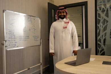 تعلم اساليب العمل والتطوير المهني، ورشات عمل تدريبية مهنية،استخدام السبورة لسهولة الشرح، رجل عربي خليجي سعودي يرتدي الثوب الابيض و الشماغ يقوم بتوضيح الخطوات لتحقيق الأهداف داخل مقر الشركة, تطوير استراتيجيات شركات السعودية