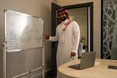 ورشات عمل تدريبية مهنية، الاشارة الى السبورة لسهولة الشرح، رجل عربي خليجي سعودي يرتدي الثوب الابيض و الشماغ يقوم بتوضيح الخطوات لتحقيق الأهداف داخل مقر الشركة, تطوير استراتيجيات شركات السعودية، تعلم اساليب العمل والتطوير المهني