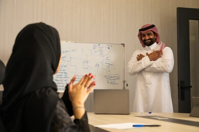 ايماءات التشجيع والتصفيق، ضمان فهم واضح وشامل للاعمال، استعمال السبورة لتوضيح العمليات والاجراءات المتبعة في الشركة، العمل الجماعي وروح الفريق، الاحترافية والتفاني في الإنجاز،امراة عربيه خليجيه سعودية محجبة تقوم بالتصفيق لزميلها