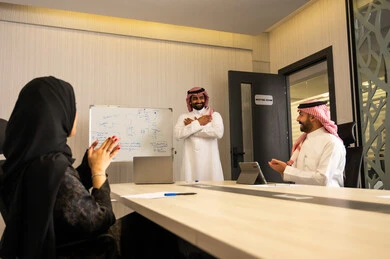 Developing plans and achieving company goals, cooperation and camaraderie among employees, collaboration and participation in completing tasks, a Saudi Arabian Gulf team consisting of a man in a white thobe and shemagh and a veiled woman wearing an abaya, clapping and congratulating their colleague.