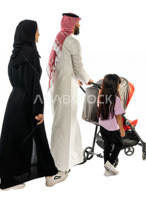 بورتريه من الخلف لرجل عربي خليجي سعودي يجرعربة الأطفال برفقة زوجته و ابنته الصغيرة بإيماءات تدل على السعادة و المحبة ، ترابط عاطفي ، مفهوم الأسرة السعيدة ، نزهة و جولة عائلية ، قضاء أوقات عائلية ممتعة