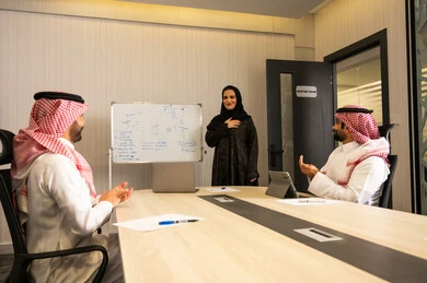 Showing appreciation during the presentation of ideas, the concept of motivation and support in the workplace, a Saudi Gulf Arab female employee explaining during a business meeting, two Saudi Gulf Arab men wearing traditional thobes and ghutras clapping, gestures of happiness and joy.