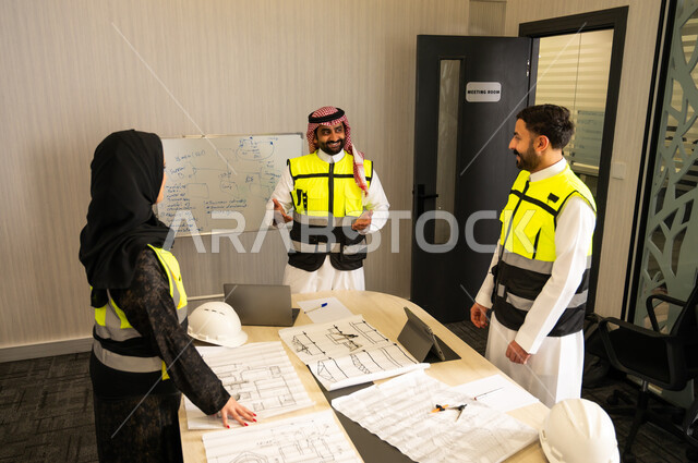 متابعة تطبيق الخطط الهندسية المعتمدة، الشركات المختصة بورشات البناء والمقاولات، التخطيط ووضع المخططات المعمارية، مجموعة مهندسون عربيون خليجيون سعوديون يردتون الثوب التقليدي و سترة الحماية يعملون على مناقشة مخطط الإنشاء وتحديد القياسات بدقة داخل مقر الشركة
