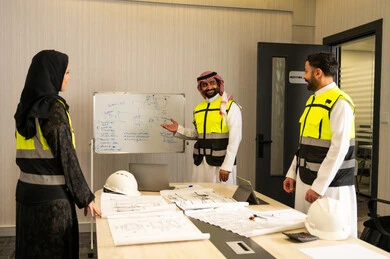 مراقبة تنفيذ الخطط الهندسية المعتمدة، الشركات المختصة بورشات البناء والمقاولات، التخطيط ووضع الرسومات المعمارية، مجموعة مهندسون عرب خليجيون سعوديون يناقشون مخطط الإنشاء وتحديد الأبعاد بدقة داخل مقر الشركة
