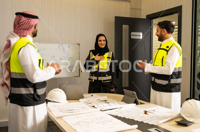 رجلان عربيان خليجيان سعوديان يرتدي الثوب التقليدي و  ستره الحماية يقومان بالتصفيق لزميلتهم، إظهار التقدير أثناء عرض الأفكار، مفهوم التحفيز والدعم في بيئة العمل