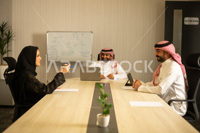 جمع البيانات و حل المشكلات، تطوير و دراسة المشاريع الجديدة, توضيح العمليات و الاجراءات المتبعة في الشركة، العمل الجماعي و التعاون، فريق عربي خليجي سعودي مكون من رجلين يرتديان الثوب التقليدي و الشماغ و سيدة محجبة ترتدي العباءة يقومان بالمناقشة, استخدام التابلت في تدوين الملاحظات