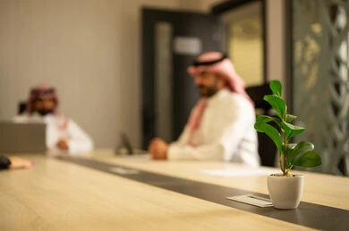 Achieving the company's goals, unity and teamwork, integrating business with technology, completing the required tasks, two Arab Gulf men from Saudi Arabia wearing traditional attire sitting in the office working on a laptop and a tablet.