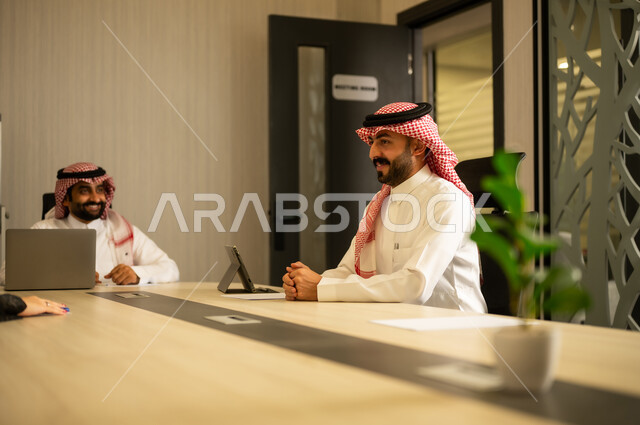 الوحدة والعمل الجماعي، دمج الأعمال مع التقنية و التكنولوجيا، إنجاز الأعمال المطلوبة، رجلان عربيان خليجيان سعوديان يرتديان الزي التقليدي يجلسانفي المكتب يعملان على الحاسب المحمول وجهاز التابلت, تحقيق أهداف الشركة