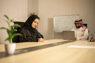 إدارة شؤون الأعمال وتنظيمها، استخدام جهاز تقني حديث ومتطور، مهنة ووظيفة ادارية مكتبية، موظف عربي خليجي سعودي يرتدي الثوب التقليدي يقوم بالعمل على الحاسوب المحمول داخل المكتب، الشركات والمكاتب في المملكة العربية السعودية، امراه عربية خليجيه سعودية محجبة ترتدي العباءة تقوم بكتابة و تدوين الملاحظات