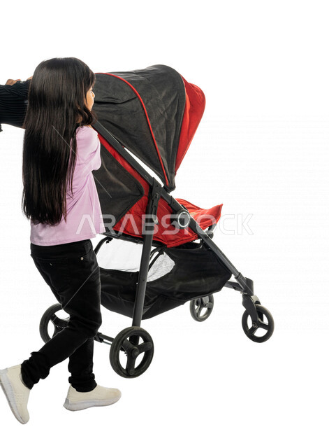 بورتريه من الخلف لطفلة عربية خليجية سعودية تمشي بجانب عربة الأطفال ، رابطة الأخوة ، ترابط عاطفي ، مفهوم الأسرة السعيدة ، نزهة و جولة عائلية ، قضاء أوقات عائلية ممتعة