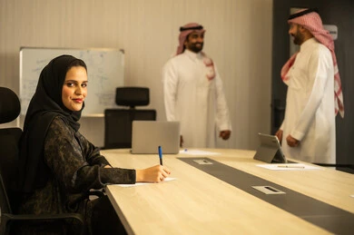 امراه عربية خليجيه سعودية محجبة ترتدي العباءة تقوم بكتابة و تدوين الملاحظات، التعاون و المشاركة في إنجاز الأعمال، تطوير الخطط وتحقيق أهداف الشركة، الحوارات و النقاشات حول المشاريع، صفقات شراكة جديدة، رجلان عربيان خليجيان سعودين يرتديان الزي التقليدي يتناقشان