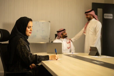 التعاون و المشاركة في إنجاز الأعمال، تطوير الخطط وتحقيق أهداف الشركة، الحوارات و النقاشات حول المشاريع، صفقات شراكة جديدة، رجلان عربيان خليجيان سعودين يرتديان الزي التقليدي يتناقشان, امراه عربية خليجيه سعودية محجبة ترتدي العباءة تقوم بكتابة و تدوين الملاحظات