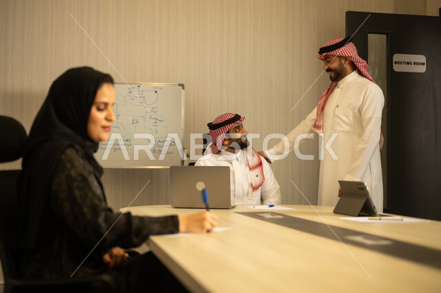 تطوير الخطط وتحقيق أهداف الشركة، الحوارات و النقاشات حول المشاريع، التعاون و المشاركة في إنجاز الأعمال، صفقات شراكة جديدة، رجلان عربيان خليجيان سعودين يرتديان الزي التقليدي يتناقشان, امراه عربية خليجيه سعودية محجبة ترتدي العباءة تقوم بكتابة و تدوين الملاحظات