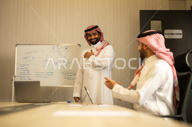 تحقيق أهداف واستراتيجيات الشركة، إيماءات الفرح والسرور، رجل عربي خليجي سعودي يرتدي الثوب و الشماغ يقوم بالتصفيق وتهنئة زميله, ورشات عمل وتدريب