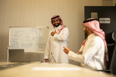 Achieving the company's goals and strategies, gestures of joy and happiness, an Arab Gulf Saudi man wearing a thobe and ghutrah clapping and congratulating his colleague, workshops and training.