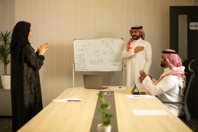 Ensuring a clear and comprehensive understanding of the work, gestures of encouragement and applause, using a whiteboard to clarify the processes and procedures followed in the company, teamwork and team spirit, professionalism and dedication to achievement, two Arab Gulf men from Saudi Arabia wearing traditional attire are applauding during the meeting.