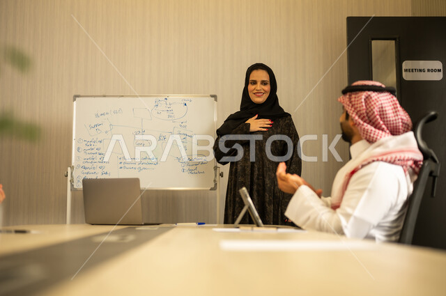 مفهوم التحفيز والدعم في بيئة العمل, إظهار التقدير أثناء عرض الأفكار, موظفة عربية خليجية سعودية  تقوم بالشرح خلال اجتماع عمل, رجل عربي خليجي سعودي يرتدي الثوب التقليدي و الشماغ يقوم بالتصفيق