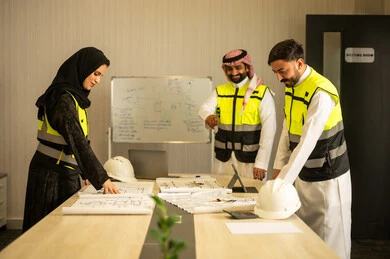Clarification of the construction plan, the concept of planning and organization, monitoring the progress of the project, professional collaboration within the engineering office, a Saudi Gulf Arab engineer wearing a ghutrah and safety vest stands with his colleagues explaining the work.