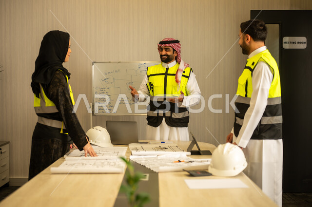 Study of the construction plan, the concept of planning and organization, monitoring the progress of the project, professional collaboration within the engineering office, a Saudi Gulf Arab engineer wearing a ghutrah and safety vest stands with his colleagues explaining the work.