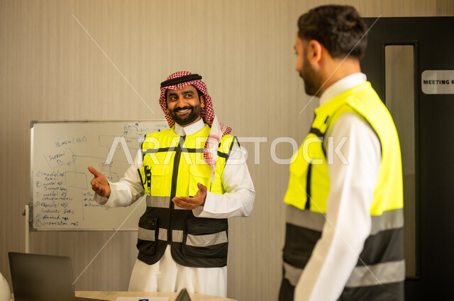 متابعة تفاصيل المشروع، مفهوم التخطيط الهندسي، مهندس عربي خليجي سعودي يرتدي سترة السلامة يقوم بشرح العمل لزميلة، بيئة عمل حديثة في قطاع الإنشاءات، مفهوم التطوير العمراني وإدارة المشاريع